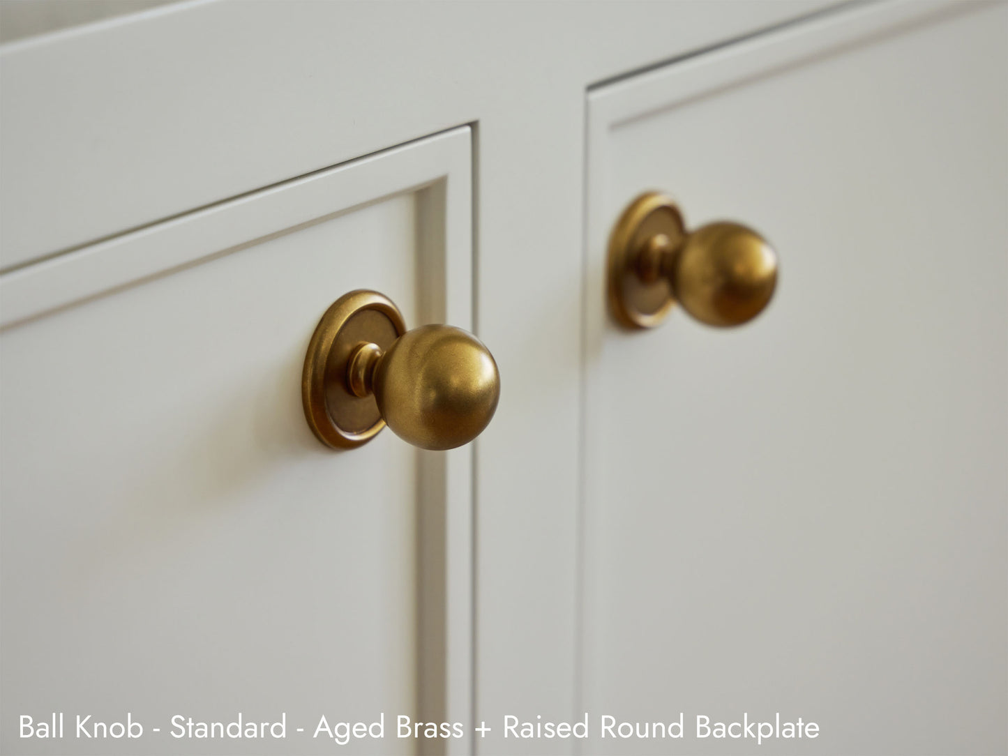 Solid brass Ball Knob in Aged Brass finish with the Raised Round Backplate installed on kitchen cabinets.