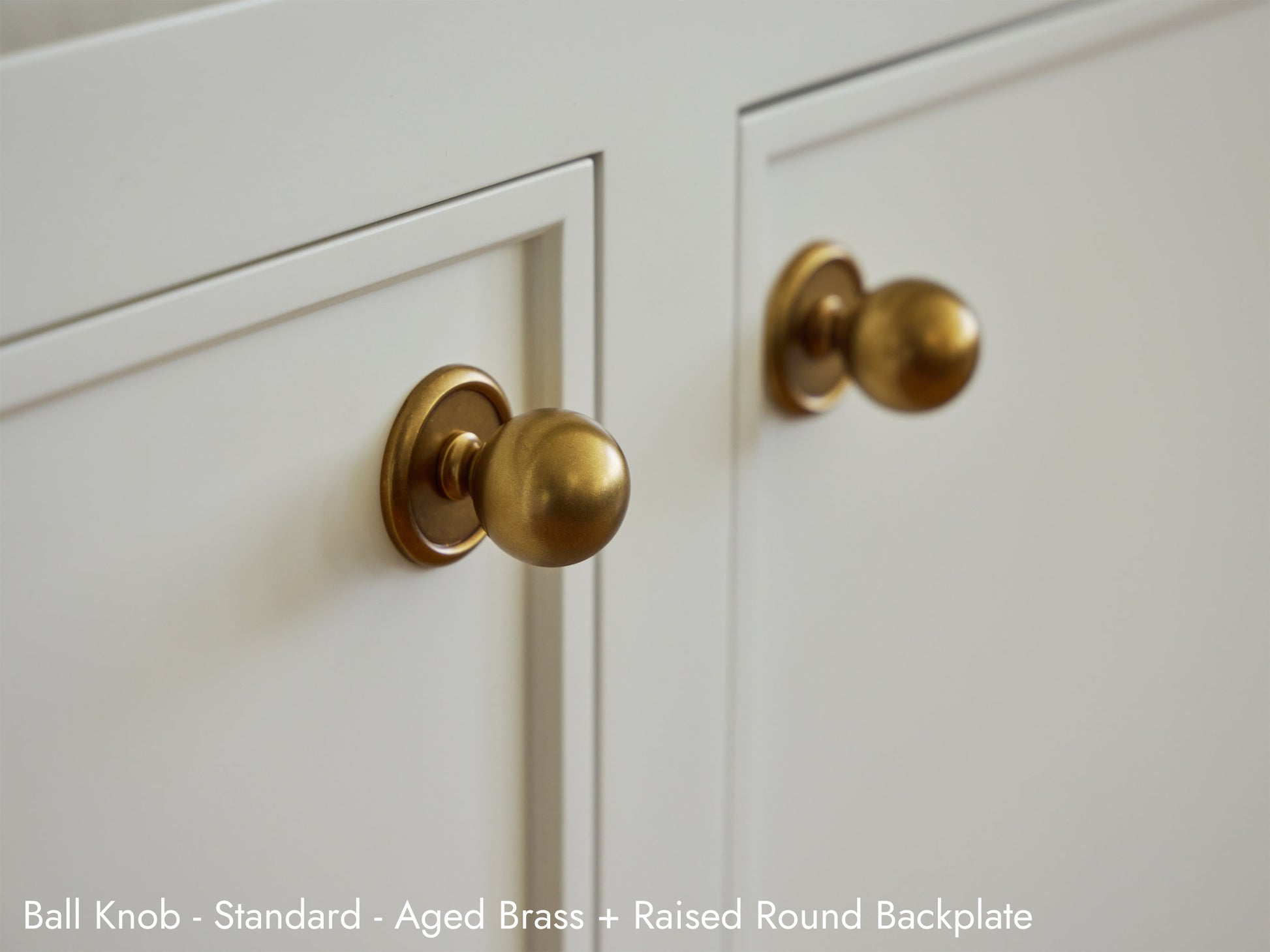 Solid brass Ball Knob in Aged Brass finish with the Raised Round Backplate installed on kitchen cabinets.