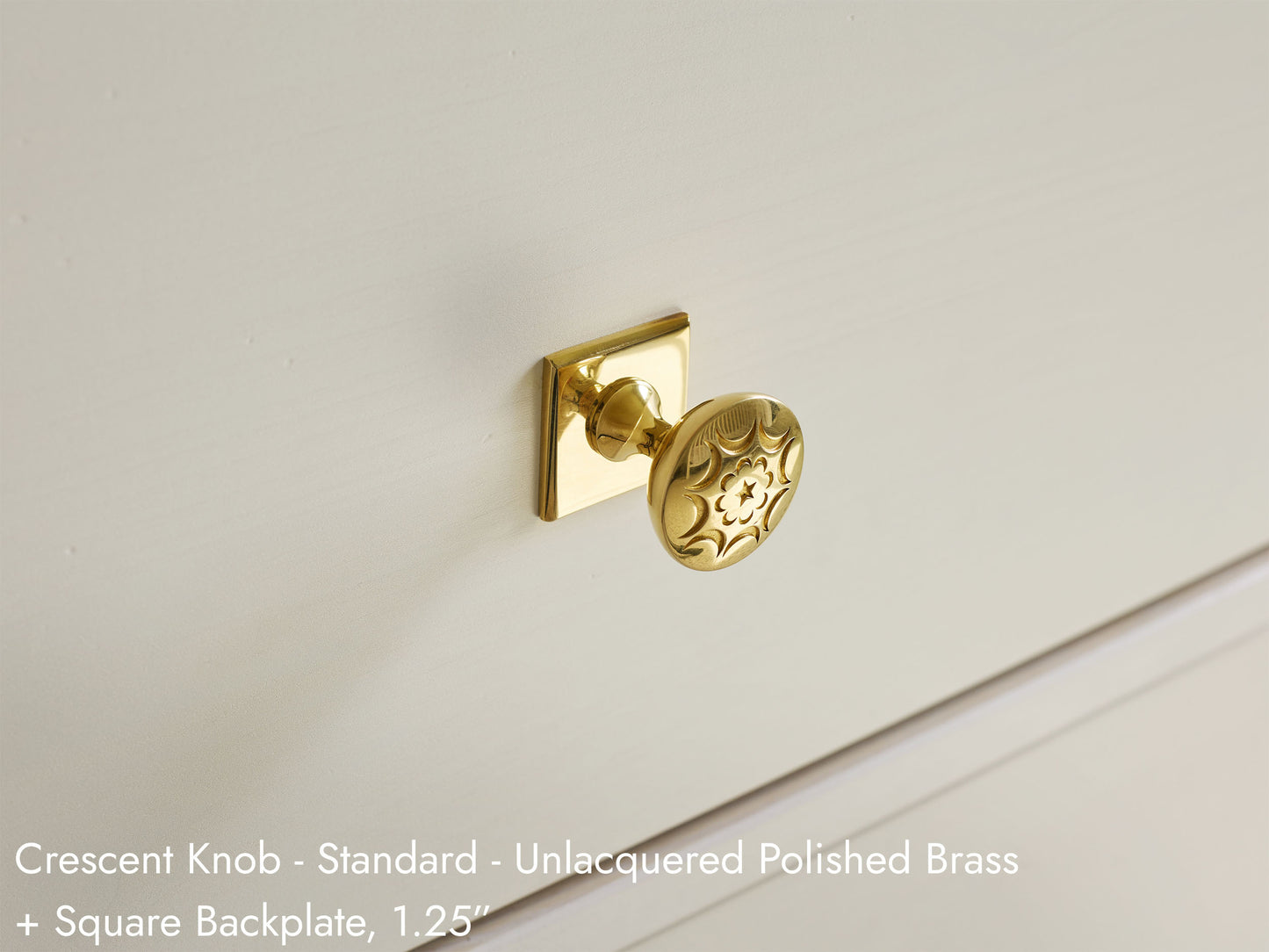 Solid brass Crescent Knob, in unlacquered polished brass finish, on cabinets with Square Backplate.