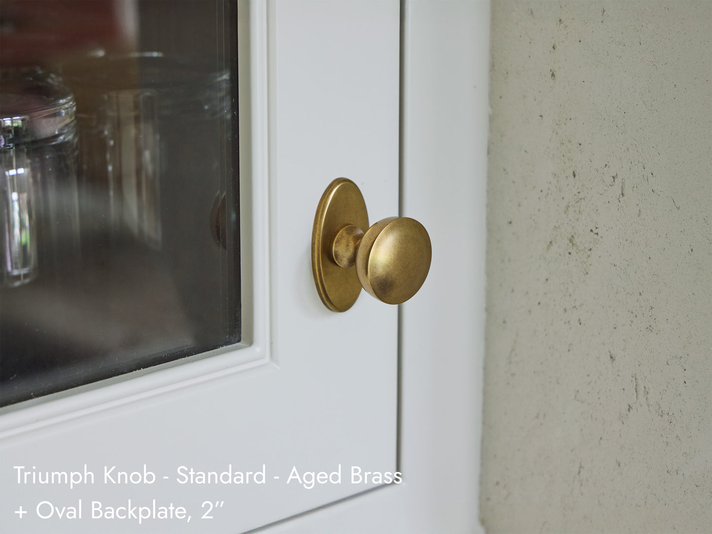 Solid brass Triumph Knob with a 2 inch Oval backplate, in aged brass, on kitchen cabinets.